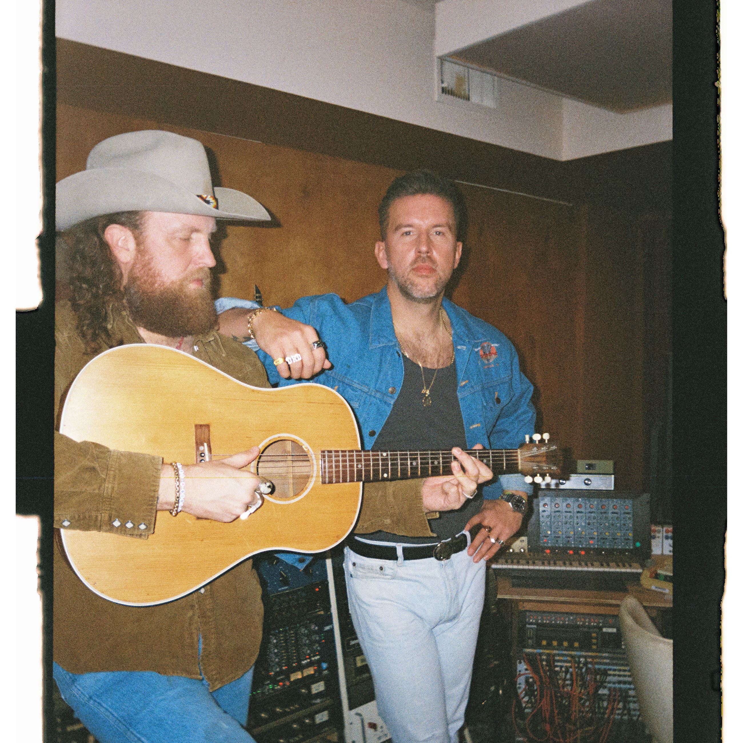 Brothers Osborne stand in front of sound equipment with guitar