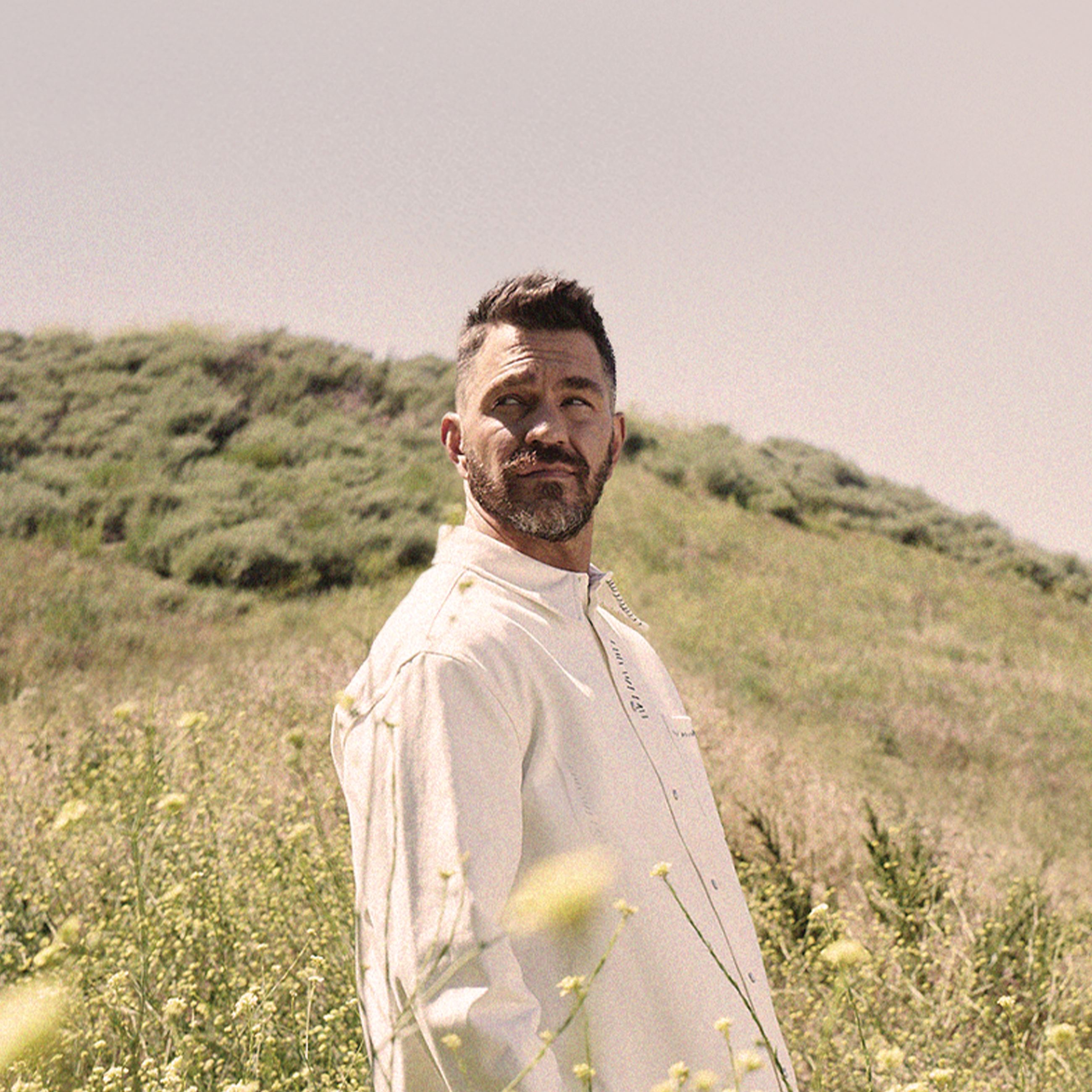 Andy Grammer standing in a field with trees and sky in the background
